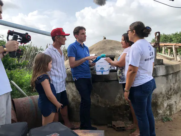 Equipe apresentando o Purafiltra a uma família ao lado da cisterna
